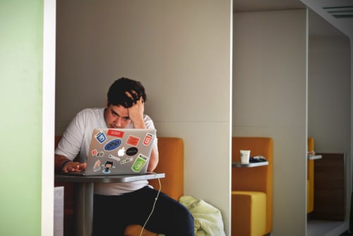 Man with head in hand looking at laptop screen