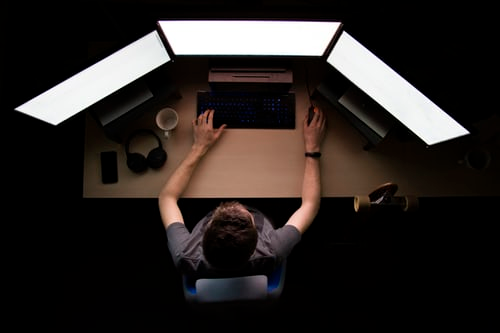 man coding on three monitors birdseye view