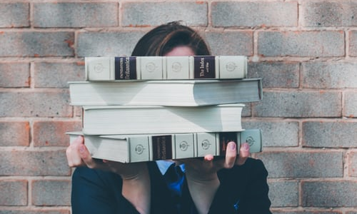 woman holding pile of books near face
