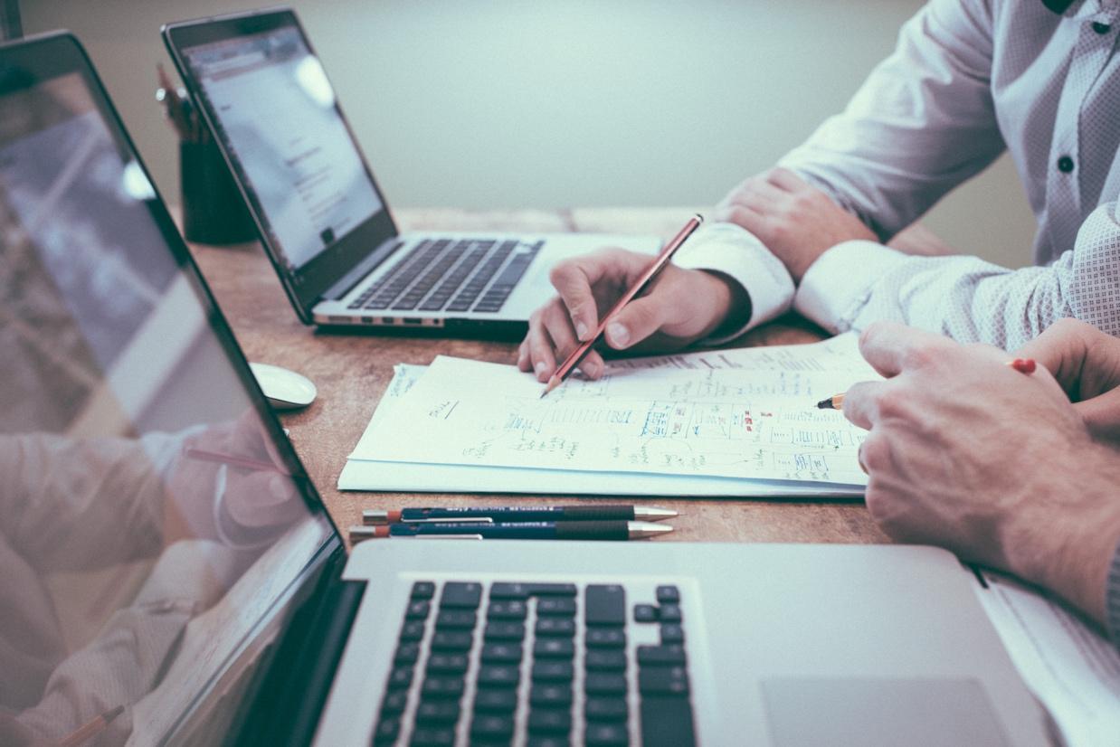 Image of two men in front of laptops, both looking at a piece of paper