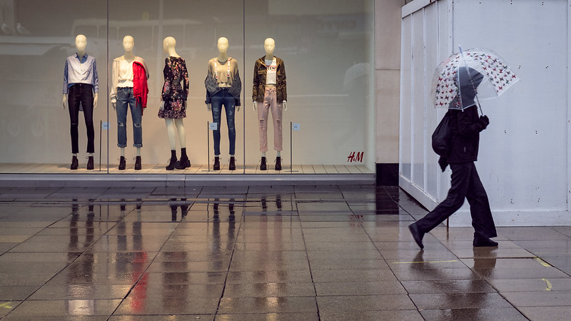 Woman in rain walking past storefront window of mannequins